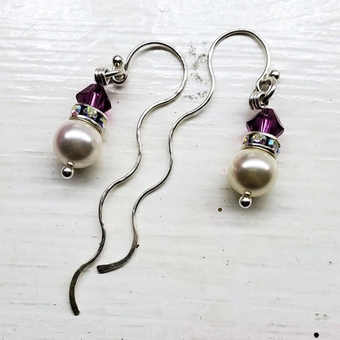 Alexa Martha Designs’ Ergonomic Crystal Pearl Wavy Ear Threaders feature sterling silver threaders with purple crystal beads, rhinestone spacers, and white pearls, elegantly displayed on a white wooden surface.