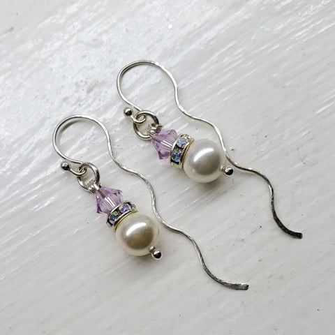 Ergonomic Crystal Pearl Wavy Ear Threaders by Alexa Martha Designs feature white pearls, light purple crystal beads, and blue crystal spacer rings, elegantly displayed on a white surface.