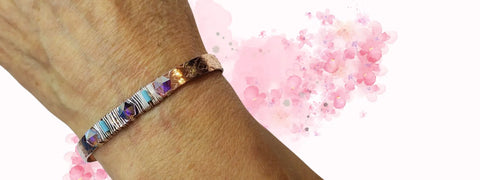A close-up of a wrist adorned with the Crystal Spike Bead Copper Cuff by Alexa Martha Designs, set against a pink watercolor floral background.