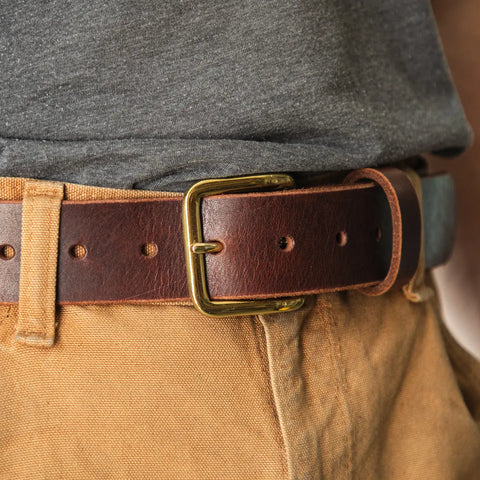 A close-up of a person wearing tan pants, a dark gray shirt, and the Homestead Brand Essential Leather Belt No. 1508 with a solid brass buckle, made in the U.S.A.