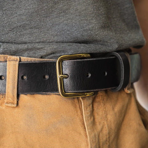 Close-up of a person wearing tan pants and a dark gray shirt with the Homestead Brand Essential Leather Belt No. 1508, featuring black leather and a solid brass buckle. Proudly made in the U.S.A.