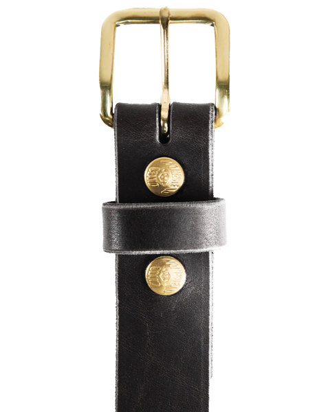 A close-up of the Homestead Brand Essential Leather Belt No. 1508 in black, featuring a solid brass buckle, two gold logo-embossed studs, and a visible belt loop securing the strap. Made in the U.S.A.