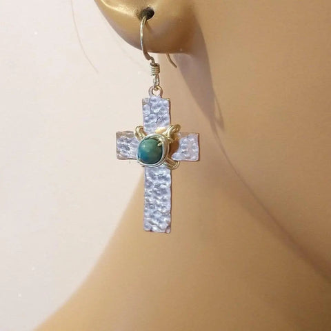 A close-up of a person wearing Alexa Martha Designs hammered copper cross earrings with turquoise beads—ideal for fans of unique, handcrafted jewelry.