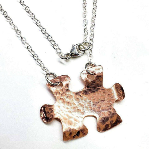 The Handmade Hammered Copper Puzzle Piece Necklace by Alexa Martha Designs features a silver chain and unique pendant—a striking handmade autism jewelry piece, displayed on a white background.