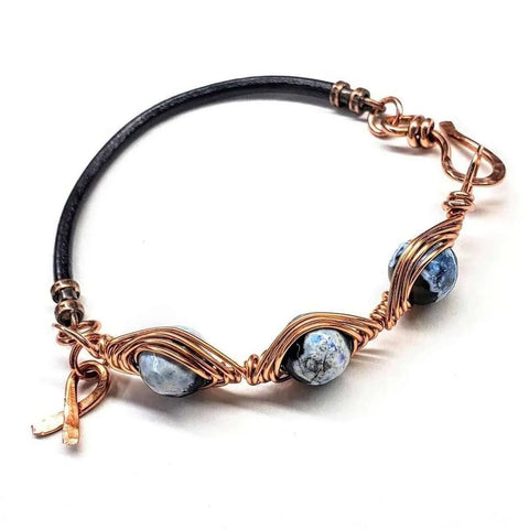 The Alexa Martha Designs Herringbone Wire Wrap Child Abuse Prevention Half Cuff Ribbon Bracelet features a handmade black leather band with three blue marbled beads and a small copper charm.