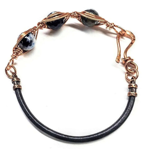 The Herringbone Wire Wrap Child Abuse Prevention Half Cuff Ribbon Bracelet by Alexa Martha Designs features a handmade Southwestern style with a black leather band, copper wire wrap, marbled beads, and a decorative hook clasp.