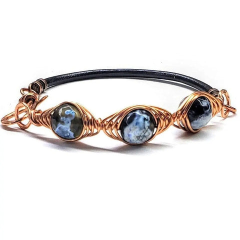 The Herringbone Wire Wrap Child Abuse Prevention Half Cuff Ribbon Bracelet by Alexa Martha Designs features three marbled blue and white stones in a handmade herringbone wire wrap on a black band with a copper clasp.