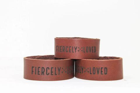 Three Fiercely Loved Cuffs by Urban Southern are stacked—two on the bottom, one on top. Handcrafted in the USA from full-grain leather, each displays FIERCELY LOVED in bold black letters on brown leather against a white background.