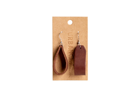 A pair of teardrop-shaped brown leather Everyday Earrings by Urban Southern with bronze-plated hooks, shown on a kraft card with URBAN visible in the background against a white backdrop. Ideal for daily wear.