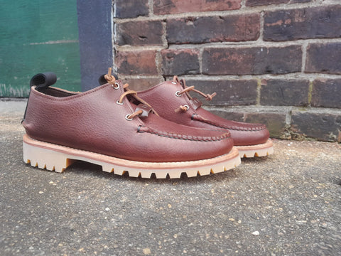 The BBH Kineo premium leather lace-up shoes with thick, light-colored rugged soles are displayed on a concrete surface in front of a brick wall and green door.