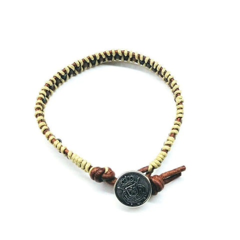 The Leather Seed Bead Rattlesnake Tail Weave Bracelet by Alexa Martha Designs features tan and brown woven cord with a round black Tree of Life engraved button clasp, shown on a white background.