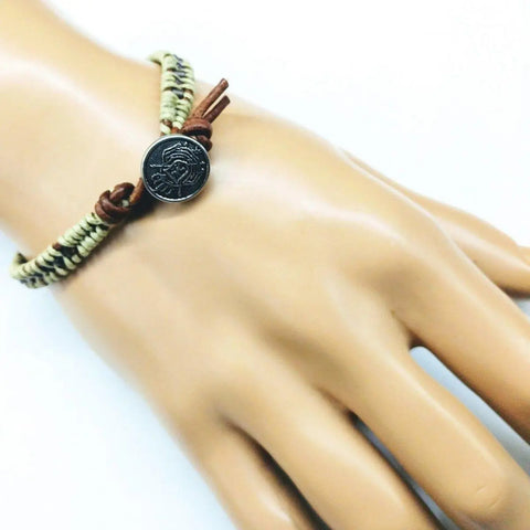A mannequin hand displays the Alexa Martha Designs Leather Seed Bead Rattlesnake Tail Weave Bracelet, featuring beige and brown leather with a round engraved Tree of Life closure, shown on a white background.