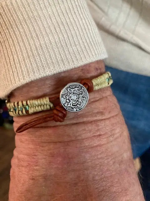 A close-up of a wrist wearing the Alexa Martha Designs Leather Seed Bead Rattlesnake Tail Weave Bracelet, shown over a light sweater and blue jeans.