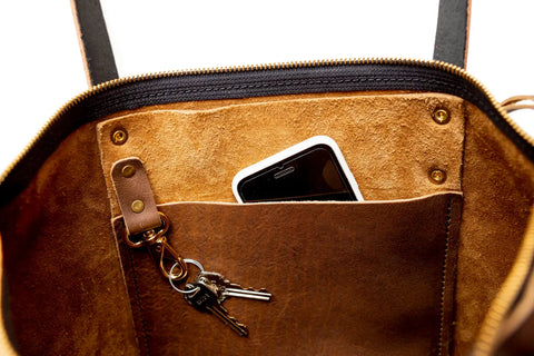 The Urban Southern Urban Zipper Tote is open, revealing a suede-lined interior pocket with a smartphone and keychain. The unzipped purse has full-grain black leather handles and showcases its spacious design.