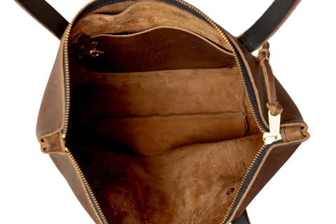The Urban Southern Urban Zipper Tote, made in America from brown full-grain leather, features a gold zipper, a roomy suede-lined interior with a side pocket, and is shown empty from above.