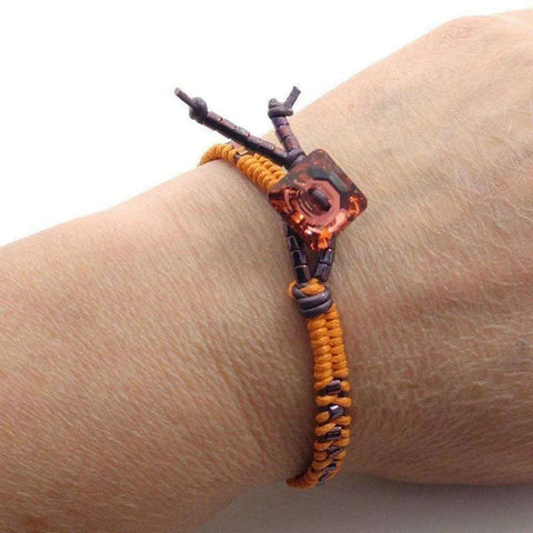 A close-up of a wrist wearing the Alexa Martha Designs Orange Purple Leather Beaded Rattlesnake Tail Weave Bracelet, featuring handmade braided leather with vibrant colors and a distinctive design.