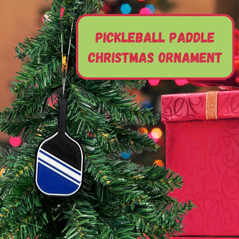 A Christmas tree with a small blue and black Chatelet Manufacturing Pickleball Paddle Christmas Ornament stands by a pink gift box. Text: “Pickleball Paddle Christmas Ornament—the perfect holiday ornament for pickleball fans.”.
