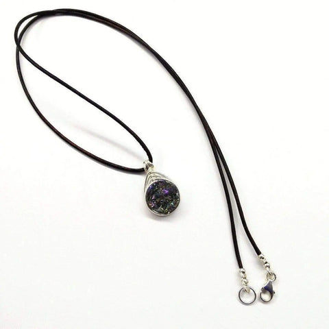 The Wire Wrapped Rainbow Druzy Necklace by Alexa Martha Designs features a teardrop-shaped, iridescent druzy stone in a sterling silver herringbone wire wrap on a thin black cord with a silver lobster clasp, displayed on a white background.