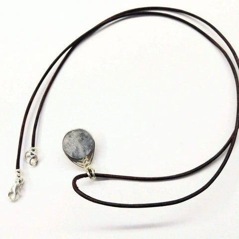 The Wire Wrapped Rainbow Druzy Necklace by Alexa Martha Designs features a thin brown leather cord, a gray oval druzy pendant in herringbone wire wrap, and a metal clasp, shown against a white background.