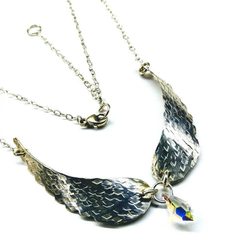 The Handmade Silver Forged Sculpted Angel Wings Necklace by Alexa Martha Designs features two textured silver wings joined with a loop, suspending a faceted teardrop crystal on a delicate chain with lobster clasp for an elegant look.