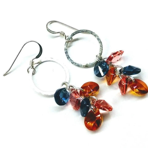 The Silver Circle Multi Color Crystal Drop Dangle Earrings by Alexa Martha Designs feature sterling silver hoops and hook-style ear wires, adorned with blue, orange, and pink teardrop crystals.