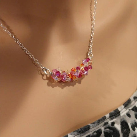 A close-up of a person wearing the Alexa Martha Designs Silver Multi Color Spring Blossom Crystal Necklace, featuring clusters of pink, orange, and clear crystals, paired with a black and white patterned top.
