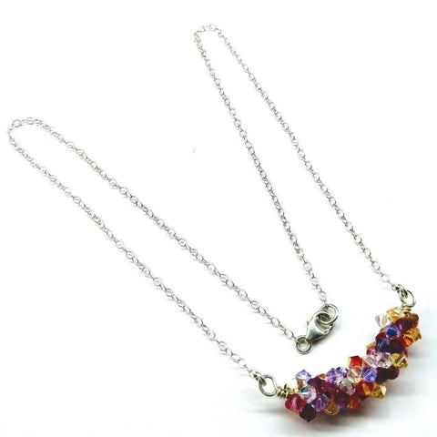 The Silver Multi Color Spring Blossom Crystal Necklace by Alexa Martha Designs features a sterling silver chain with a curved row of faceted orange, purple, and clear crystals—a stunning handmade piece.