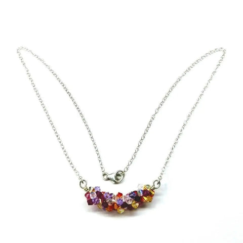 The Silver Multi Color Spring Blossom Crystal Necklace by Alexa Martha Designs features a sterling silver chain and a curved cluster of red, purple, orange, and clear Swarovski crystals, finished with a simple clasp.