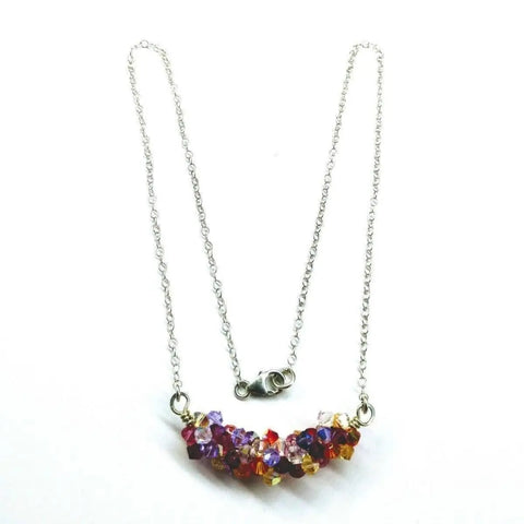 The Silver Multi Color Spring Blossom Crystal Necklace by Alexa Martha Designs features a curved cluster of small red, purple, yellow, and pink crystals on a sterling silver chain—a vibrant handmade jewelry piece.