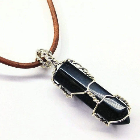 The Silver Wire Wrapped Gemstone Crystal Point Pendant by Alexa Martha Designs features a pointed crystal wrapped in sterling silver, suspended from a brown leather necklace.