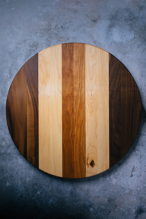 The Lazy Susan by Montana Block features a handcrafted round solid wood tabletop with alternating light and dark vertical grain stripes, set on a textured gray concrete base—an eye-catching centerpiece for any table.