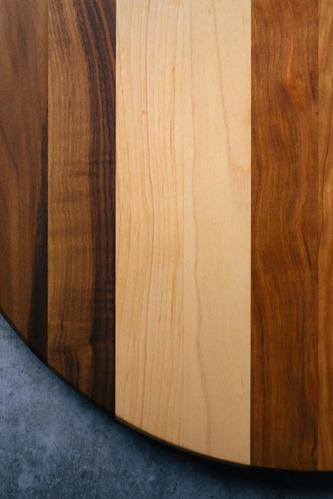 The Lazy Susan by Montana Block is a handcrafted, round solid wood turntable with alternating light and dark vertical stripes, set against a gray textured background.