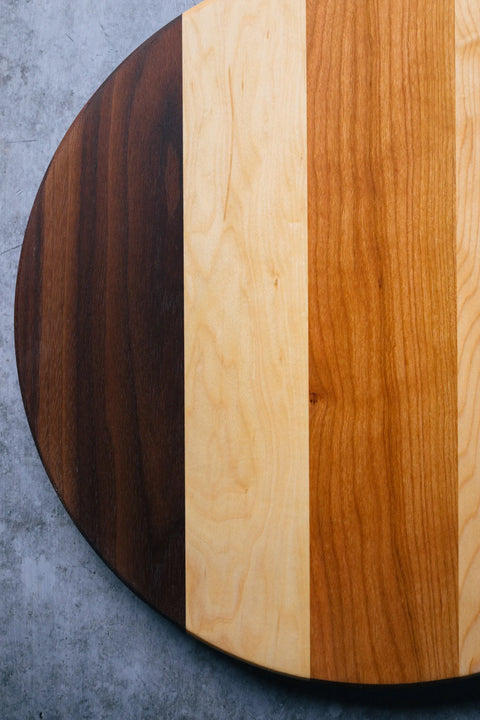 The Lazy Susan by Montana Block features an oval, handcrafted solid wood top with three vertical sections—dark brown, light beige, and medium honey tones—set against a gray concrete background.