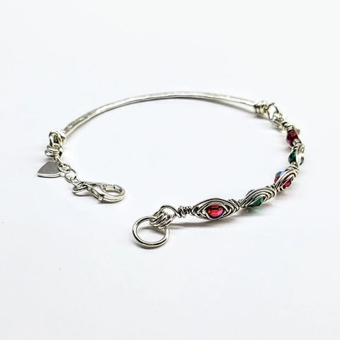 The Limited Edition Silver Wire Wrapped Red Green Christmas Holiday Tube Bracelet by Alexa Martha Designs features festive beads, a heart charm, and lobster clasp—perfect for the holidays. Shown on a white background.