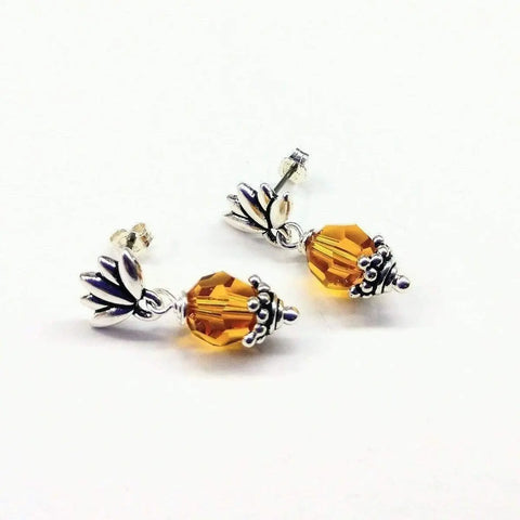 The Sterling Silver Crystal Pineapple Studded Earrings by Alexa Martha Designs are handmade stud earrings featuring faceted amber-colored beads and silver-toned caps, displayed on a white background.