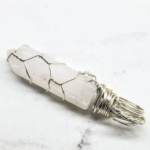 The Alexa Martha Designs Sterling Silver Messy Wire Wrap Gemstone Pointed Crystal Pendant features a clear hexagonal crystal wrapped in sterling silver wire with a loop for hanging, displayed on a white surface.
