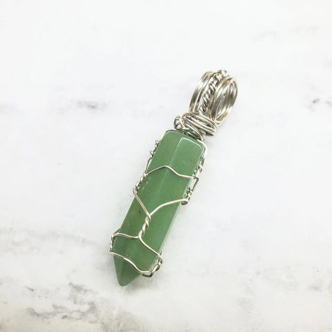 The Sterling Silver Messy Wire Wrap Gemstone Pointed Crystal Pendant by Alexa Martha Designs features a stylish spiral bail, beautifully showcased on a white marble background.