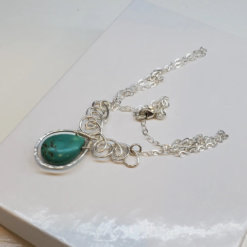The As Seen on TV Turquoise Drop Sterling Silver Wire Wrapped Necklace by Alexa Martha Designs features a teardrop turquoise pendant with intricate wire wrapping, showcasing Montana-made artisanal elegance. Displayed beautifully on a white surface.