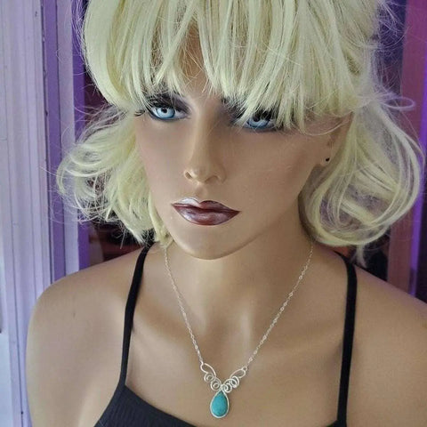 A blonde, blue-eyed mannequin wears the Alexa Martha Designs As Seen on TV Turquoise Drop Sterling Silver Wire Wrapped Necklace and a black spaghetti strap top, standing before a purple-lit background.