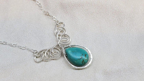 The As Seen on TV Turquoise Drop Sterling Silver Wire Wrapped Necklace by Alexa Martha Designs, featuring a teardrop turquoise pendant, is displayed on a light beige fabric background.