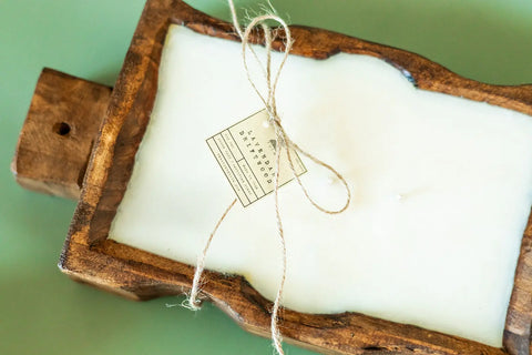 The Shanti + Tula Handcrafted Trough 3-Wick Candle is made in the USA with soy wax and comes in a reusable wood bowl, finished with a twine bow and label. It’s an artisan-crafted piece perfect for display on any surface.