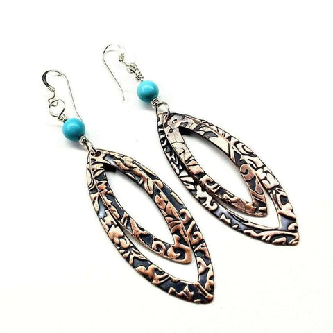 The Turquoise Copper Embossed Pointed Oval Earrings by Alexa Martha Designs feature handmade copper with embossed patterns, turquoise bead accents, and sterling silver ear wires for comfort.