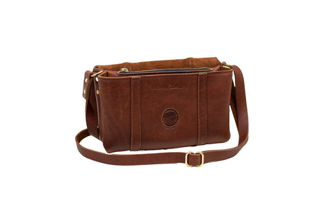 The Carriage Crossbody by Urban Southern is a brown leather bag with zipper closure, adjustable strap, and subtle front embossed logo, handcrafted in the USA and shown on a white background.