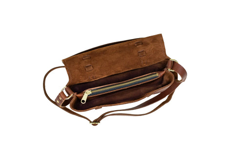 The Urban Southern Carriage Crossbody is a vintage-style brown suede leather bag with a flap, zippered pocket, and adjustable strap. Handcrafted in the USA, it features a matching brown lined interior and is shown on a white background.