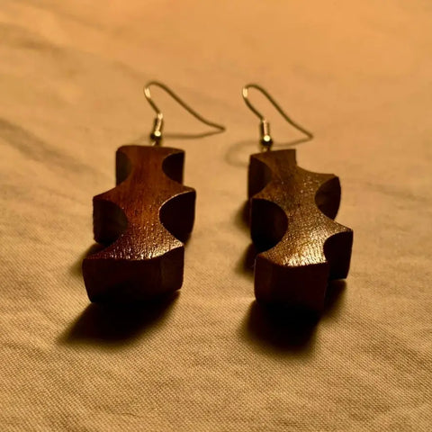 The Thorn Earring by Shop Cat Woodworks: handcrafted walnut wood earrings with a unique zigzag cutout, displayed on beige fabric under warm lighting—ideal for eco-conscious jewelry lovers.