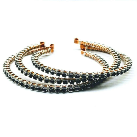 Three Wire Wrapped Copper Silver Black Crystal Rhinestone Bangles by Alexa Martha Designs, featuring jet black rhinestones on a shiny gold-toned base, are arranged in a semi-circle on a white background.