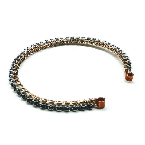 The Wire Wrapped Copper Silver Black Crystal Rhinestone Bangle by Alexa Martha Designs features intertwined copper and silver wire with sparkling black crystals, creating an elegant handcrafted look on a sleek open bangle.