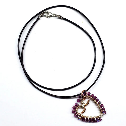 The Wire Wrapped Open Heart Crystal Necklace by Alexa Martha Designs features a heart-shaped, open-center pendant with a delicate wire swirl, purple crystal beads, black cord, and a metallic hook clasp.