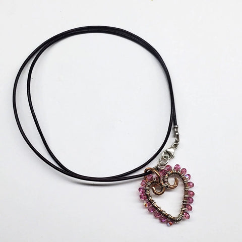 The Alexa Martha Designs Wire Wrapped Open Heart Crystal Necklace features a heart-shaped pendant with crystal accents and copper wire on a black cord, displayed against a white background.