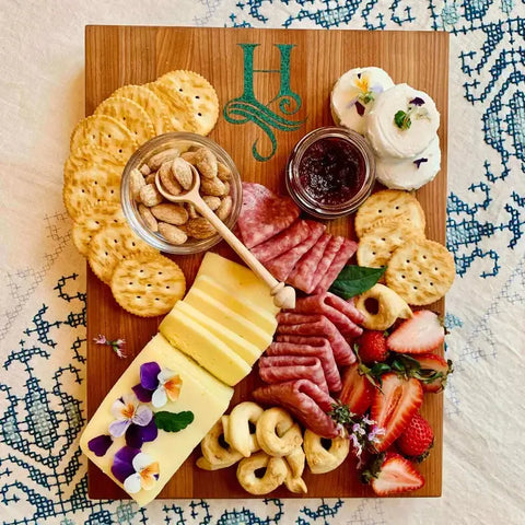 A stylish charcuterie spread of crackers, cheeses, meats, nuts, and fruit is beautifully arranged on a Handcrafted Wooden Cutting Board by Words with Boards, featuring a personalized stone-inlay monogram. Made in the USA.
